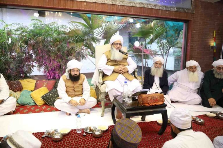 Shaykh Muhammad Mohsin Munawar Yousafi delivering an impassioned lecture, hands raised in emphasis, wearing a white turban, black vest, and glasses.