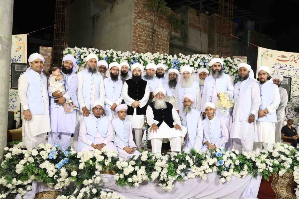 Shaykh Muhammad Mohsin Munawar Yousafi, the esteemed Islamic spiritual guide (Murshid), giving a discourse into a microphone, hands gesturing, wearing a white turban and dark vest.