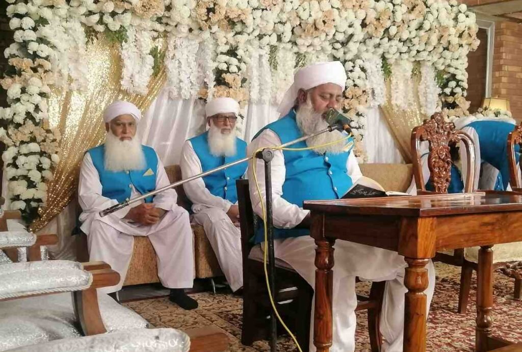 Shaykh Muhammad Mohsin Munawar Yousafi, the esteemed Islamic spiritual guide (Murshid), delivering a passionate discourse, seated and wearing a white turban and dark vest.