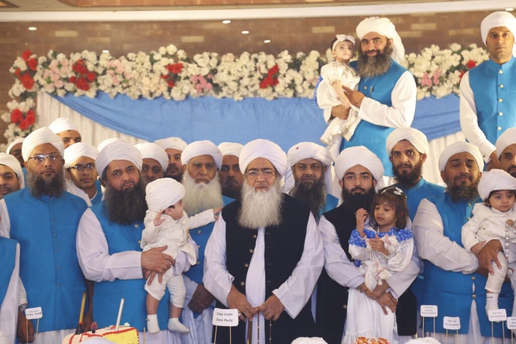 Formal group portrait of Shaykh Muhammad Mohsin Munawar Yousafi and a large assembly of scholars and students wearing matching blue vests, emphasizing the generational lineage and unity of the institution.