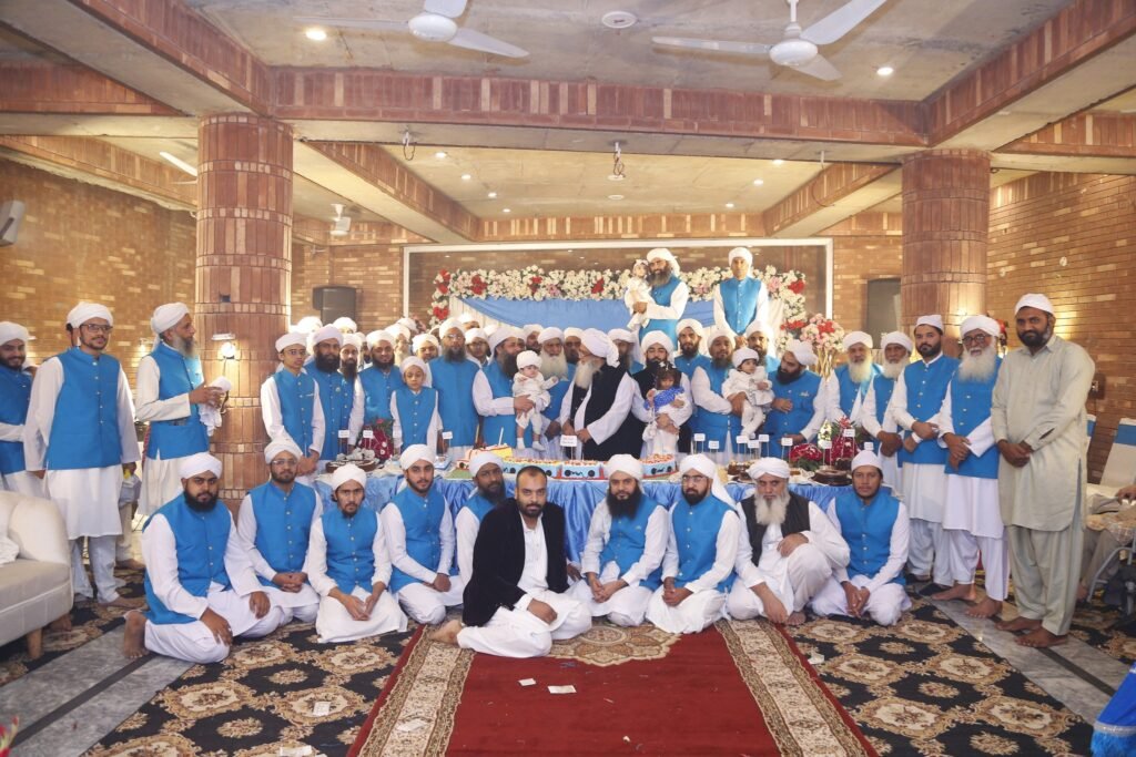Formal group portrait of Shaykh Muhammad Mohsin Munawar Yousafi and a large assembly of scholars and students wearing matching blue vests, gathered during a formal institutional celebration.